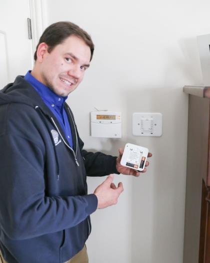 Air-Rite technician holding a new thermostat beside the old one in a customer's home